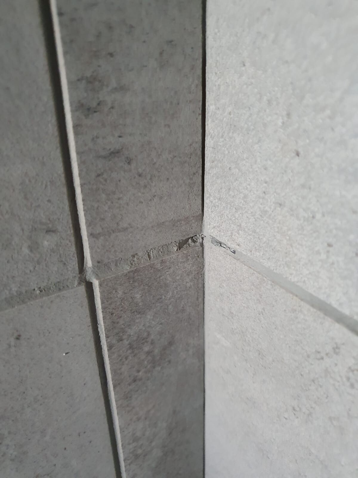 Ecke aus grauen Fliesen/Betonplatten mit sichtbaren Fugen an der Wandseite