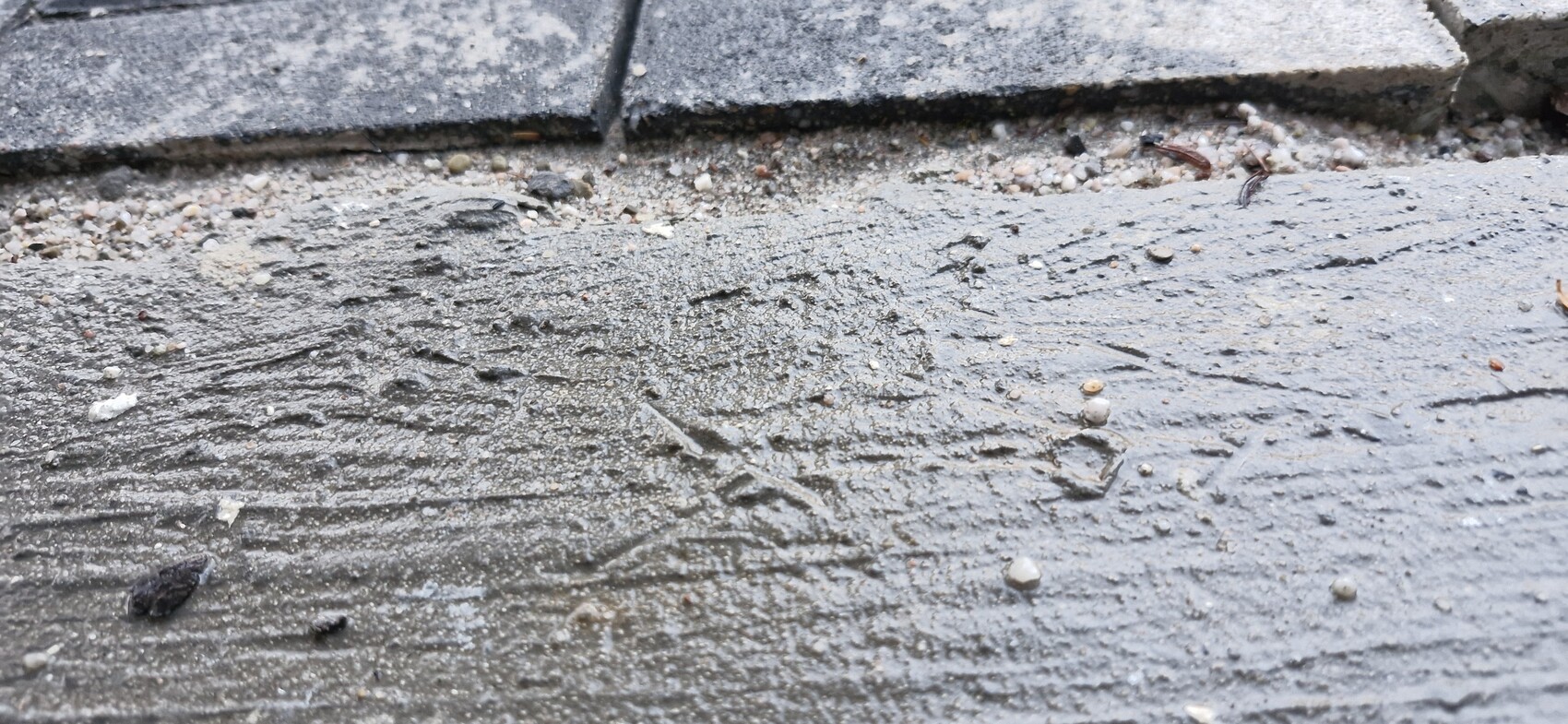 Näherer Blick auf rauen Betonboden mit Kies, am oberen Rand liegen Steinplatten.