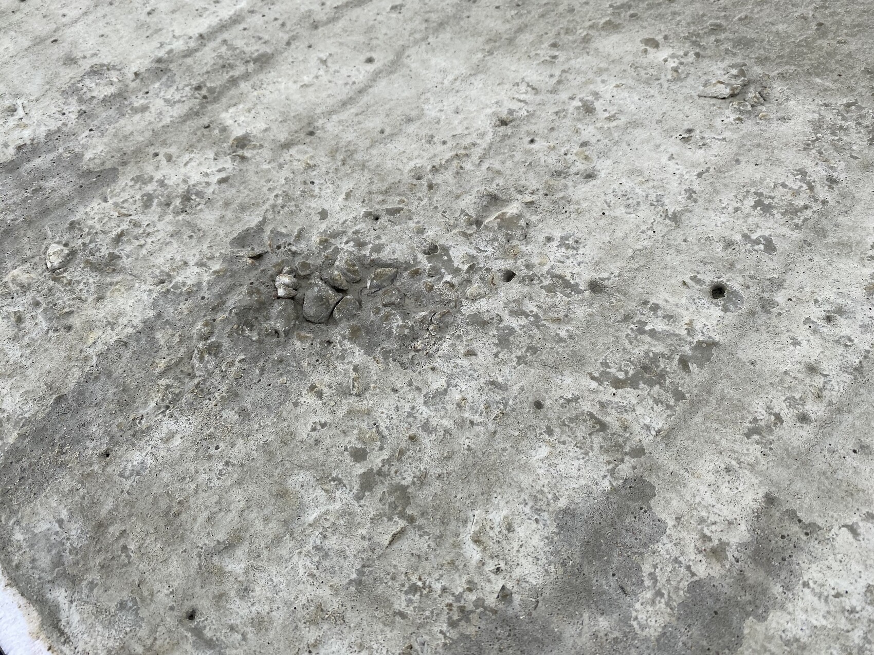 Raues Betonboden mit einer kleinen Steinansammlung, zahlreichen Poren und grauer Oberfläche.