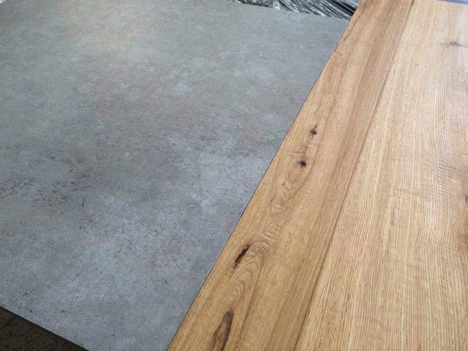 Holzplatten-Tischkante rechts neben grauem Betonboden, sichtbare Nägel.