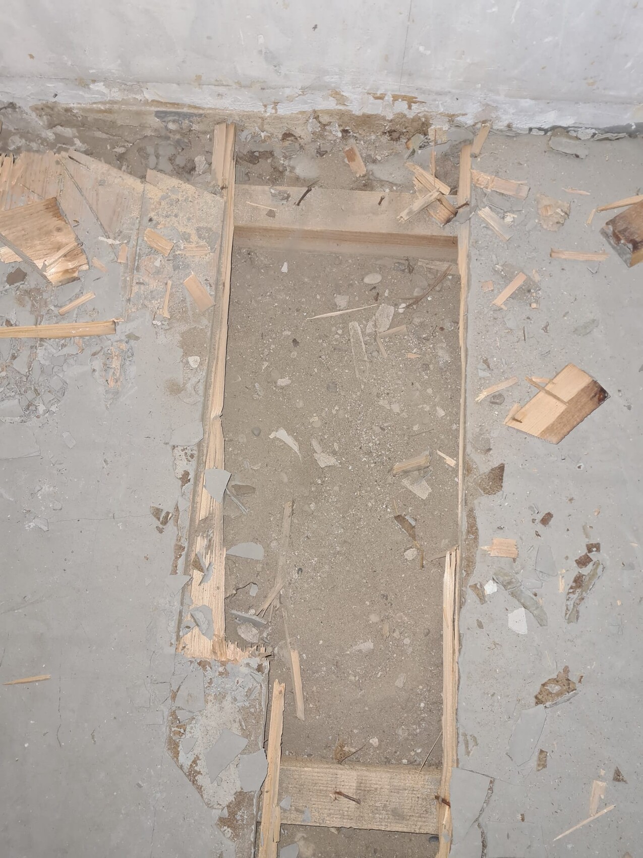 Offene rechteckige Grube im Betonboden, eingerahmt von Holzleisten, Staub und Holzspäne drumherum.
