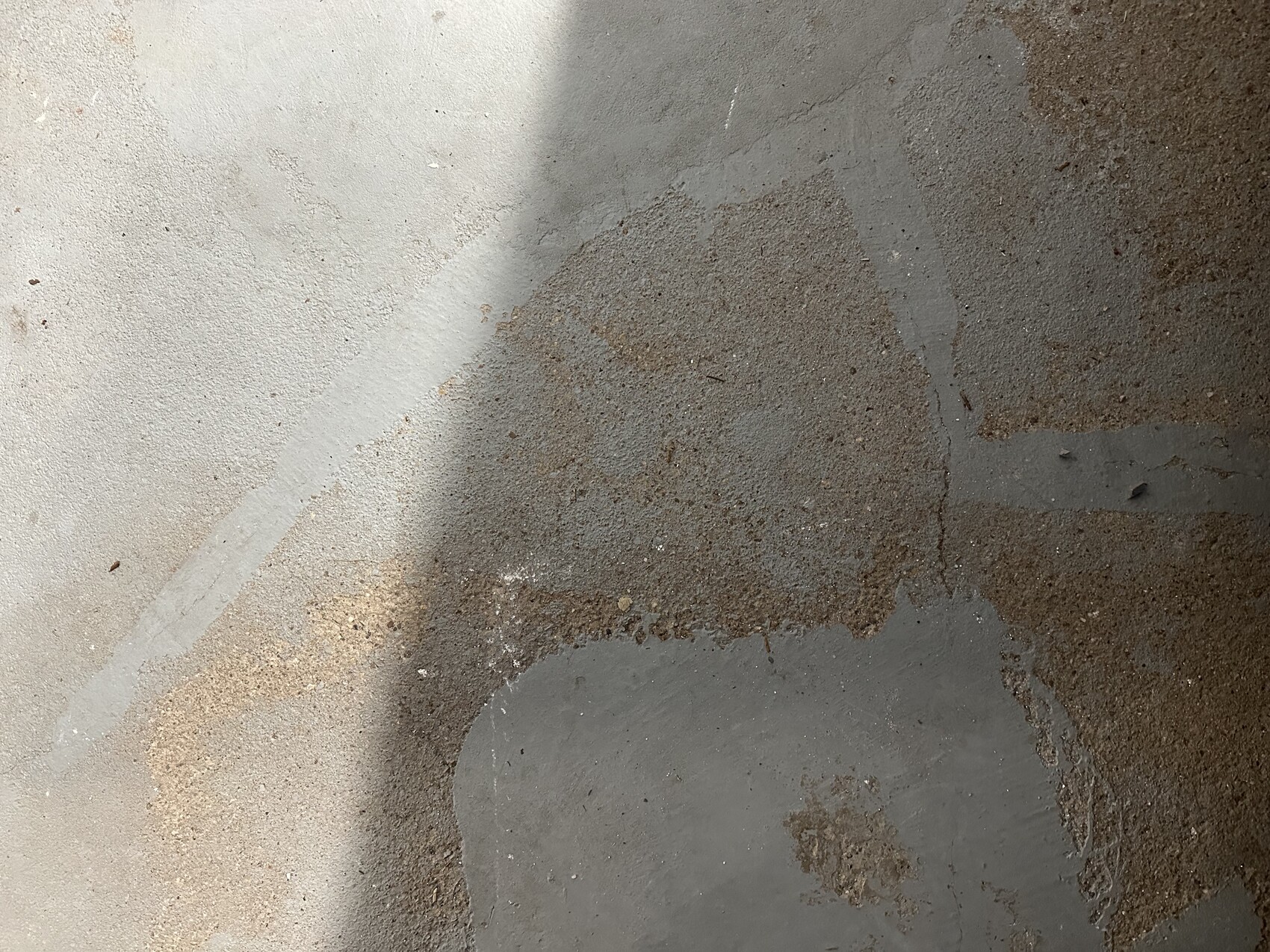 Nahaufnahme eines betonierten Bodens mit grauen Flecken, braunen Rostflecken und Schatten.
