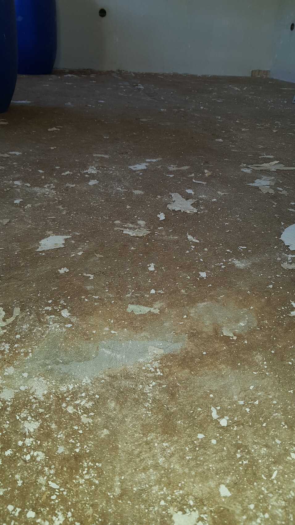 Boden mit abblätternder brauner Farbe und Putzfetzen; linkes blaues Fass im Raum.