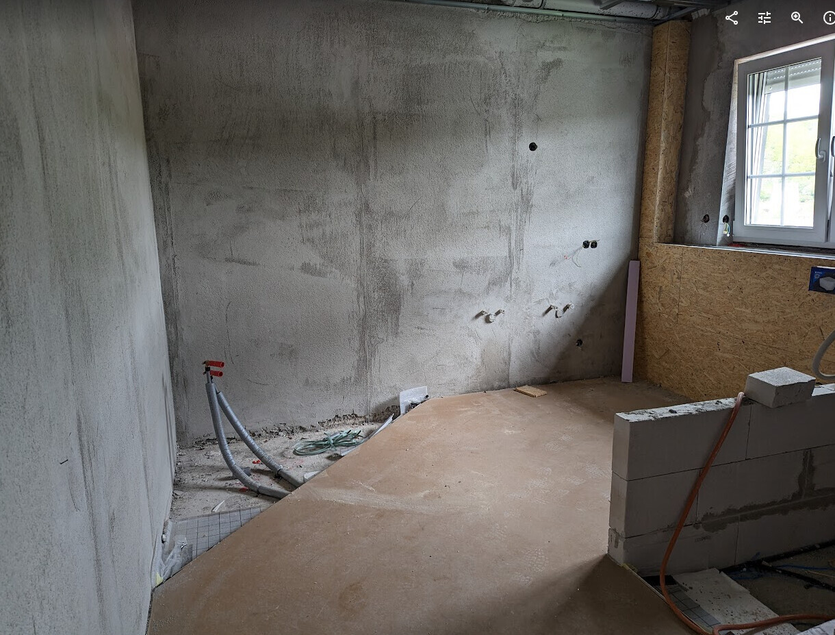 Unbearbeiteter Innenraum einer Baustelle: Rohbetonwände, Kabel, Fenster rechts.
