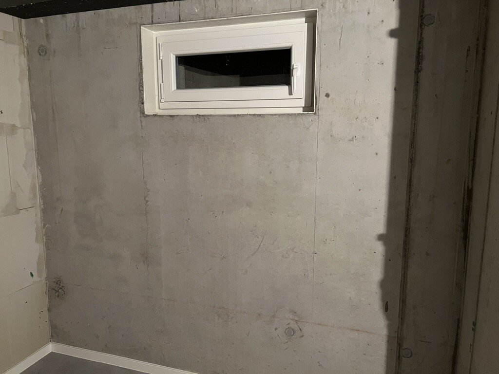 Kleines weißes horizontales Fenster in roher Betonwand eines Kellers.