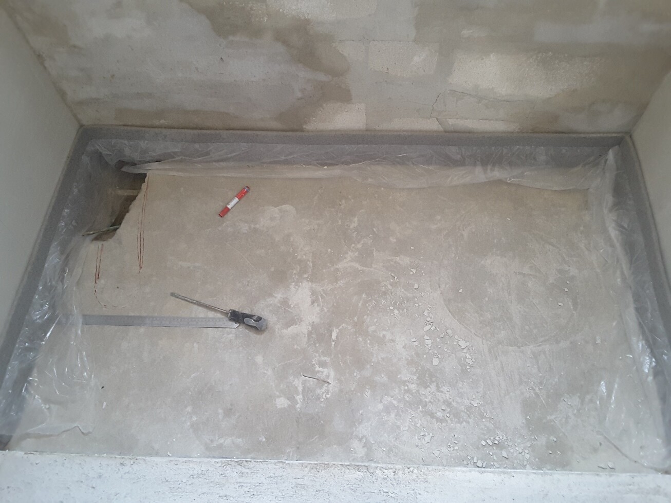 Rohbau-Badbereich mit Betonboden, unfertigen Wänden und Werkzeug im Innenraum