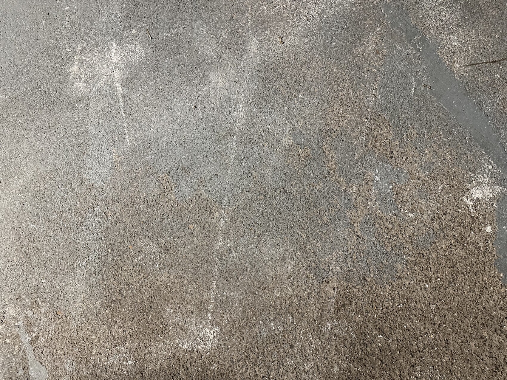 Betonboden mit grauen Flecken, Staub und braunen Rostflecken, grob strukturierte Oberfläche.