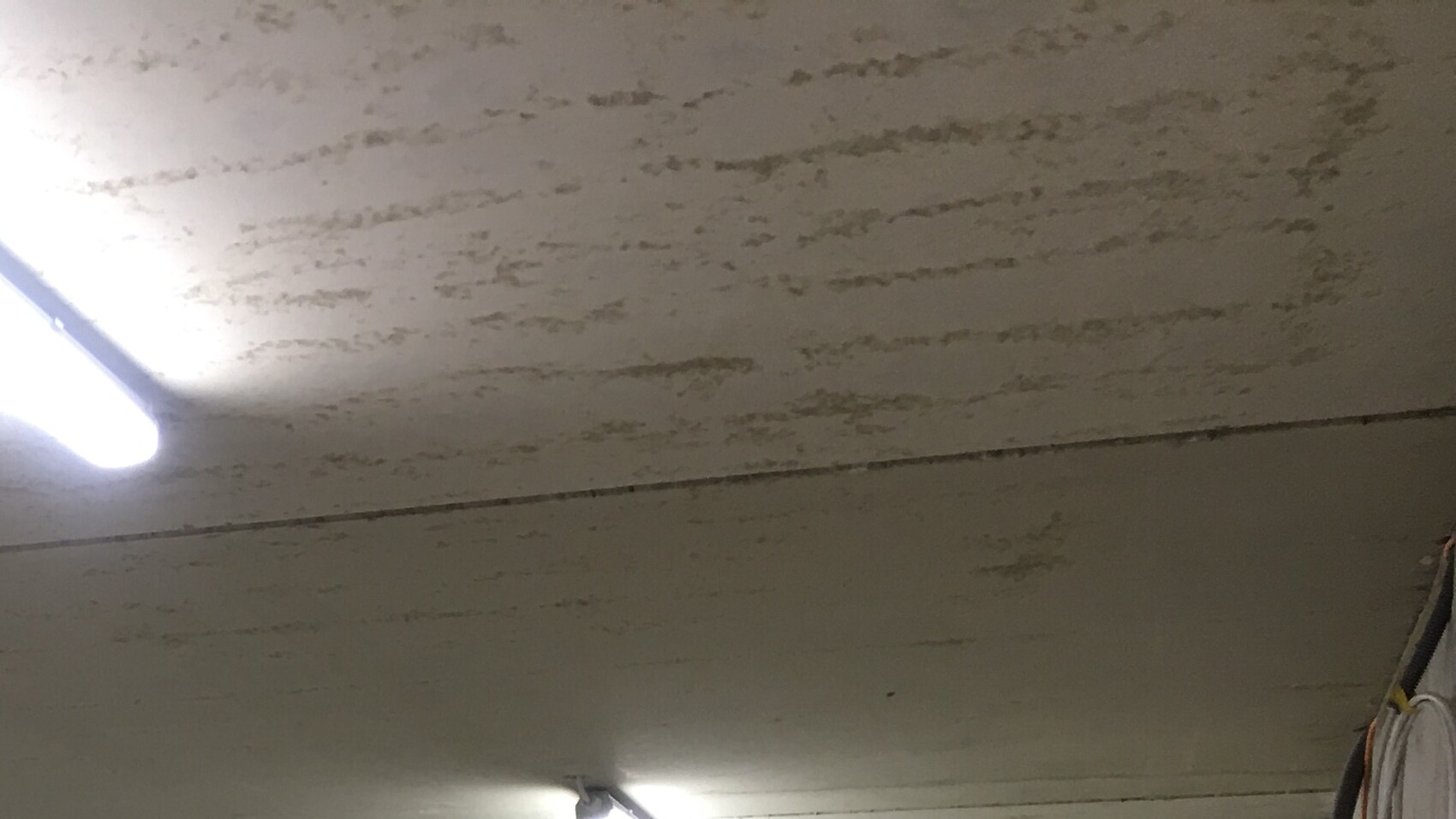 Raue, verputzte Beton-Decke mit einer langen Leuchtstofflampe links; rechts hängen Gegenstände.