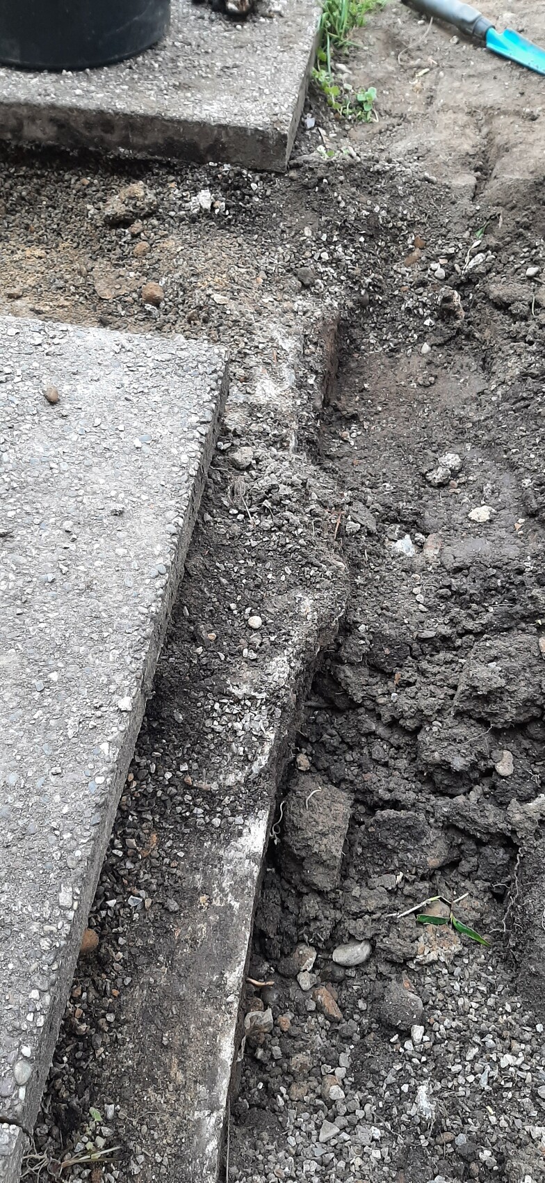 Ausgehobene Baugrube neben Betonstufe auf Baustelle mit losem Erdreich