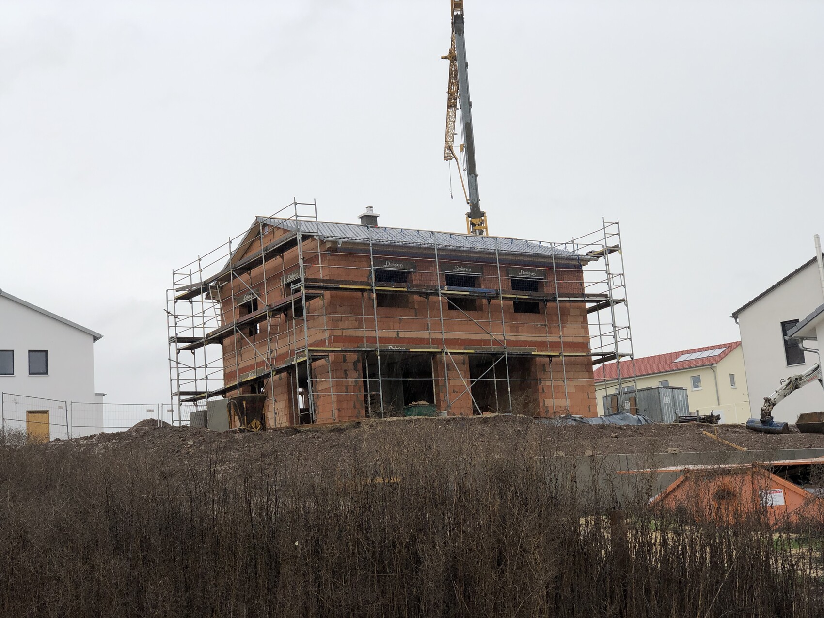 Zweistöckiges Backstein-Rohbauhaus mit Gerüst und Baukran auf einer Baustelle.