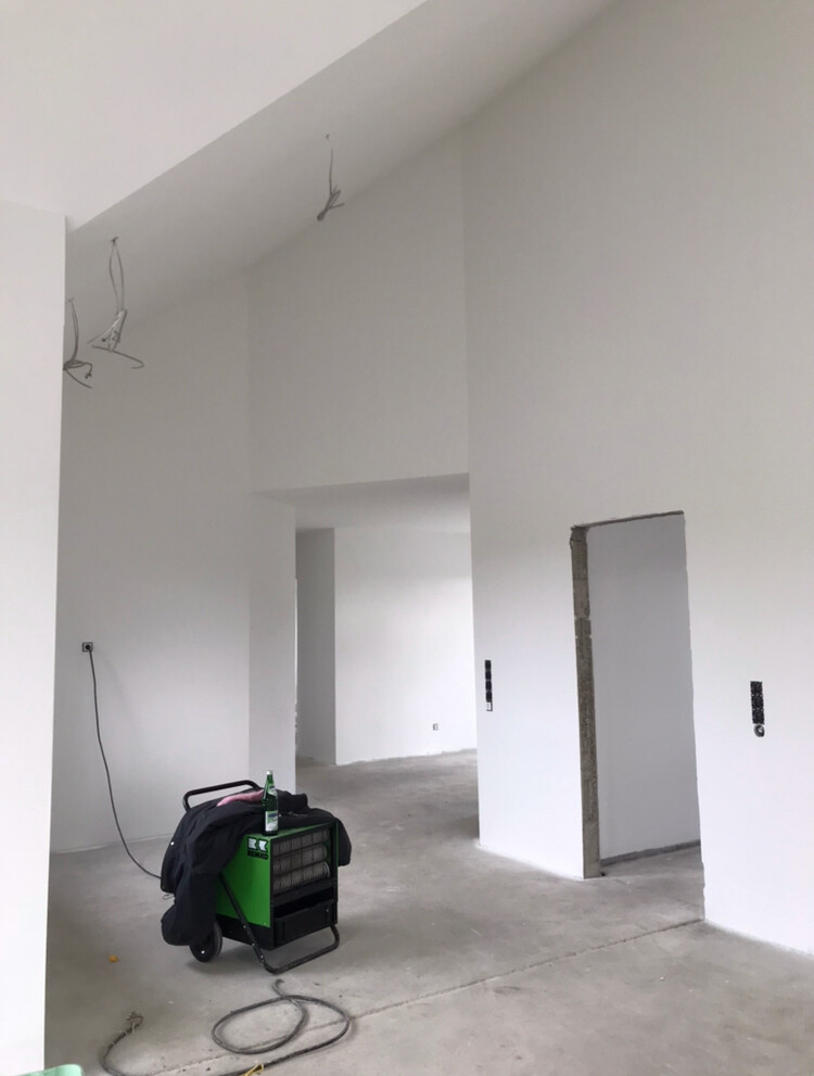 Leerer Innenraum eines Bauprojekts mit grünem Heizgerät, Kabeln, Jacke und Flasche.