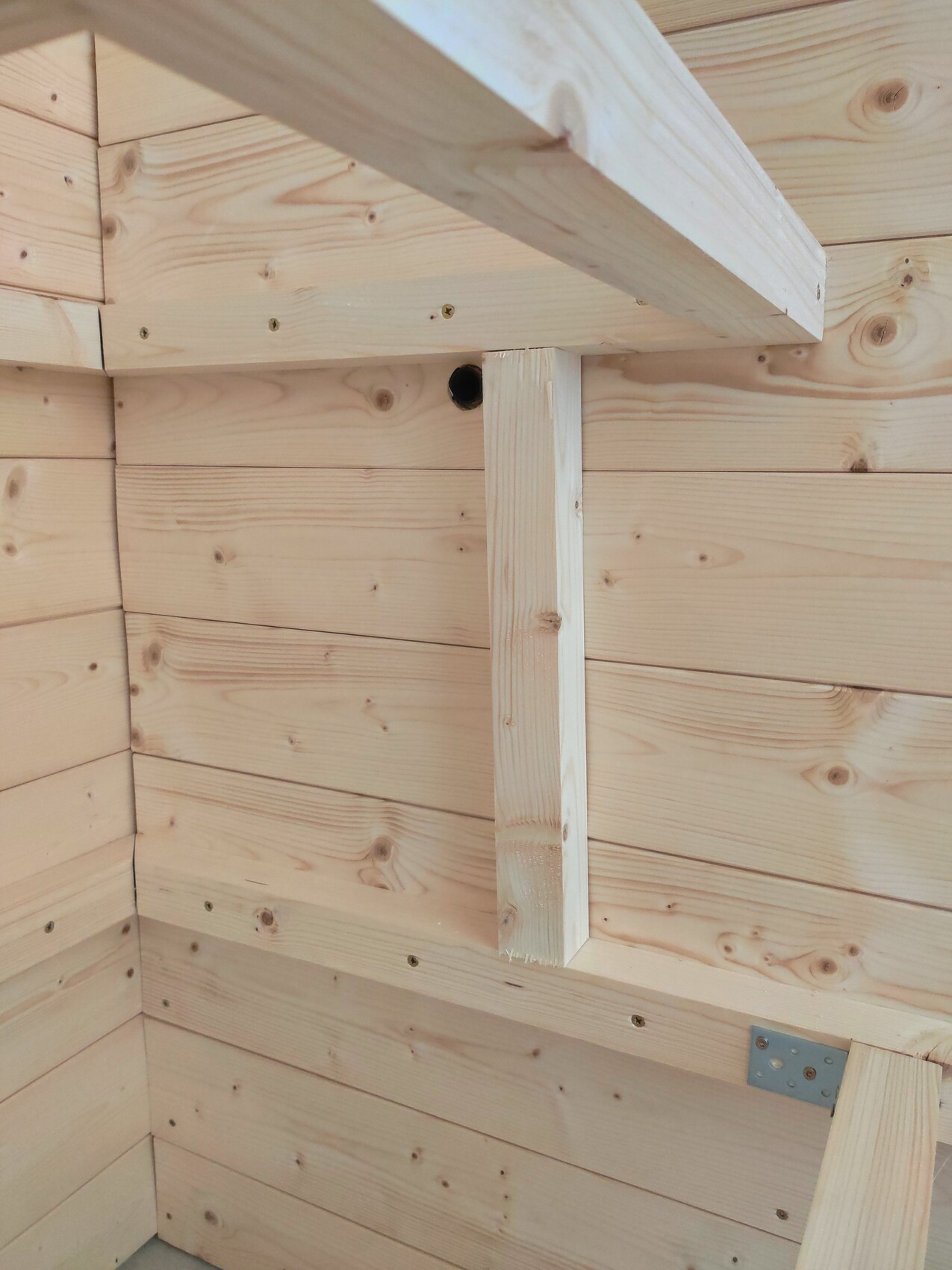 Innenansicht einer Holzwand mit hellen Holzbrettern, Querbalken und Loch in der Wand.