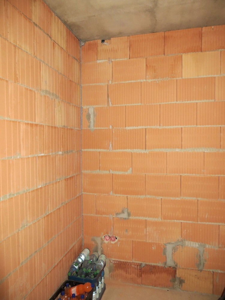 Unfertiger Raum mit Ziegelwänden, Ecke, Rohren; Flaschenkiste am Boden.