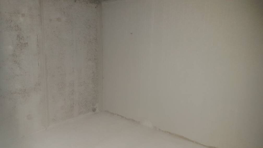 Ecke eines unfertigen Raums: grob verputzte linke Wand, glatte rechte Wand, staubiger Boden.