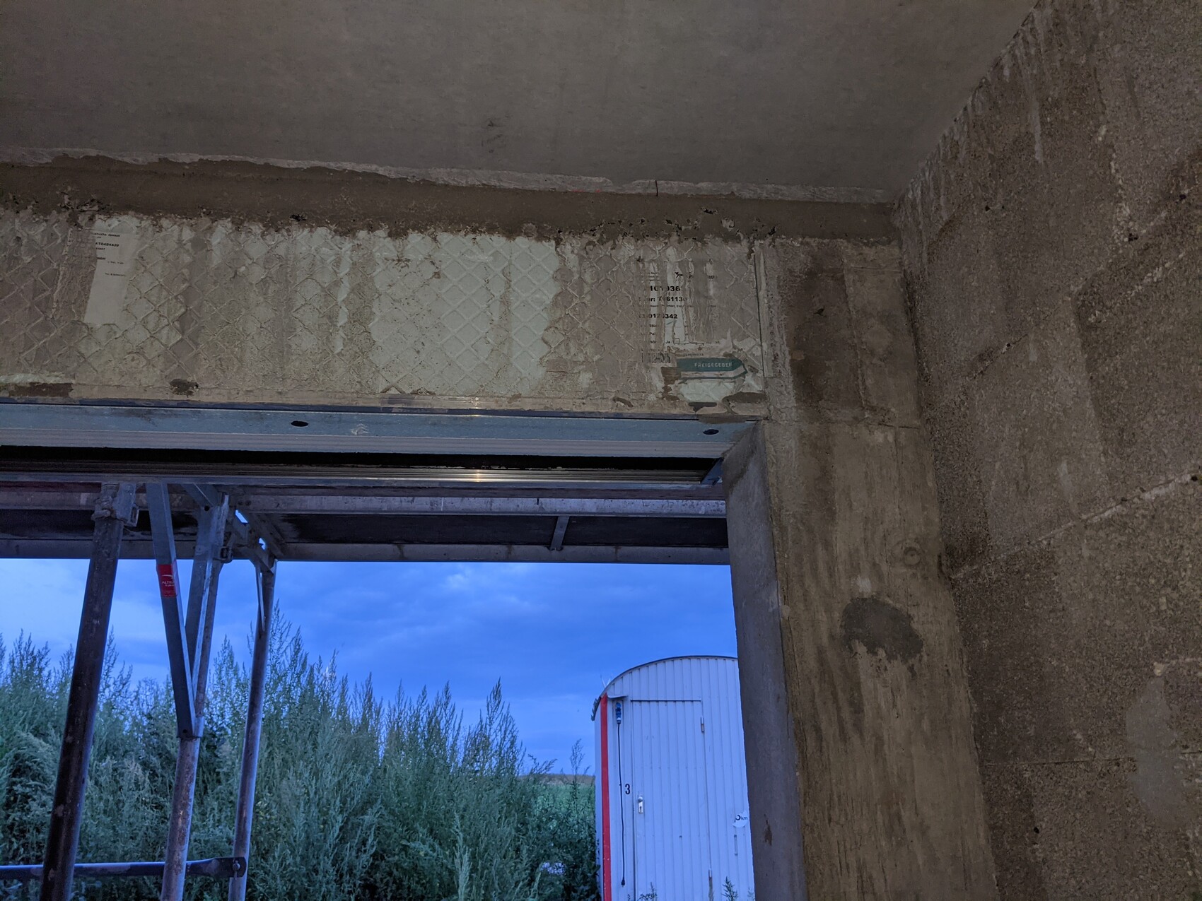 Unfertiger Betonbau: Blick nach draußen durch Türöffnung, Gerüst links, blauer Himmel.