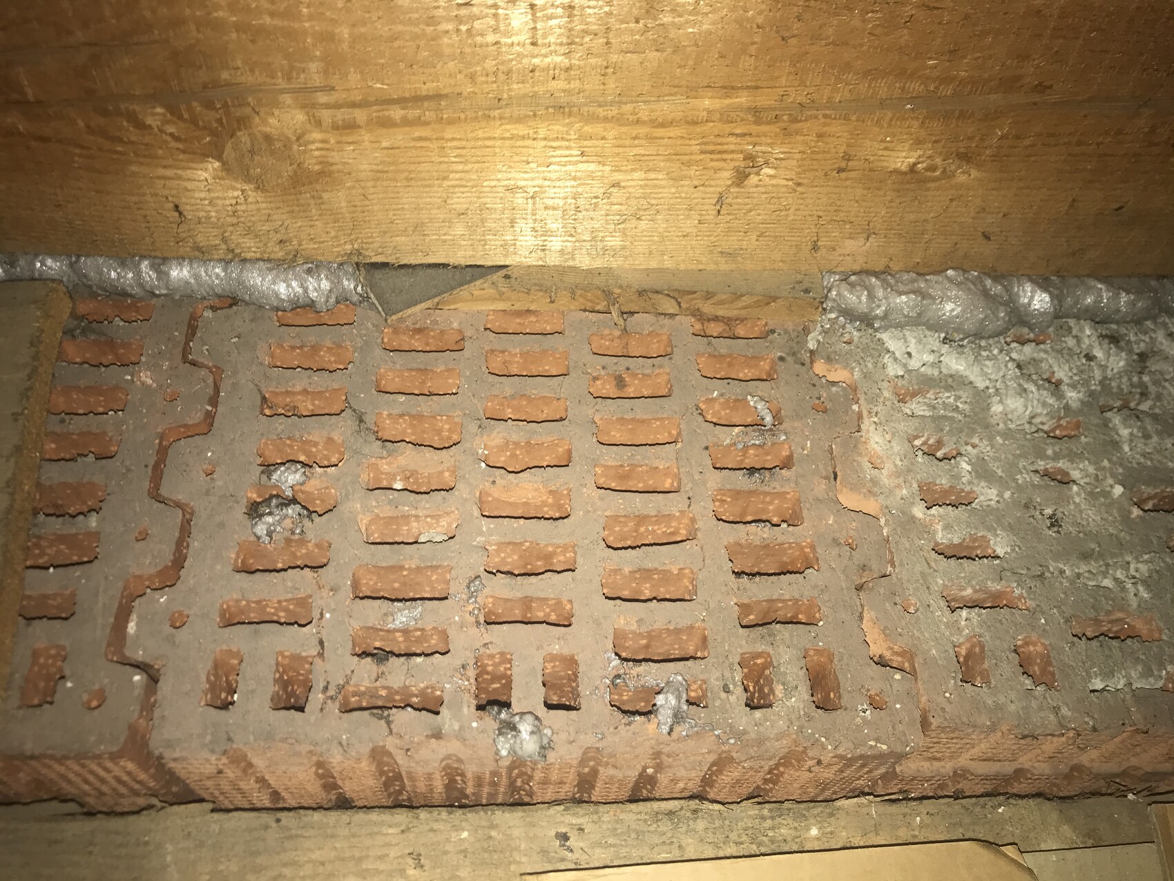 Tonziegelplatte mit rechteckigen Belüftungsöffnungen, Holzbalken und Mörtel.