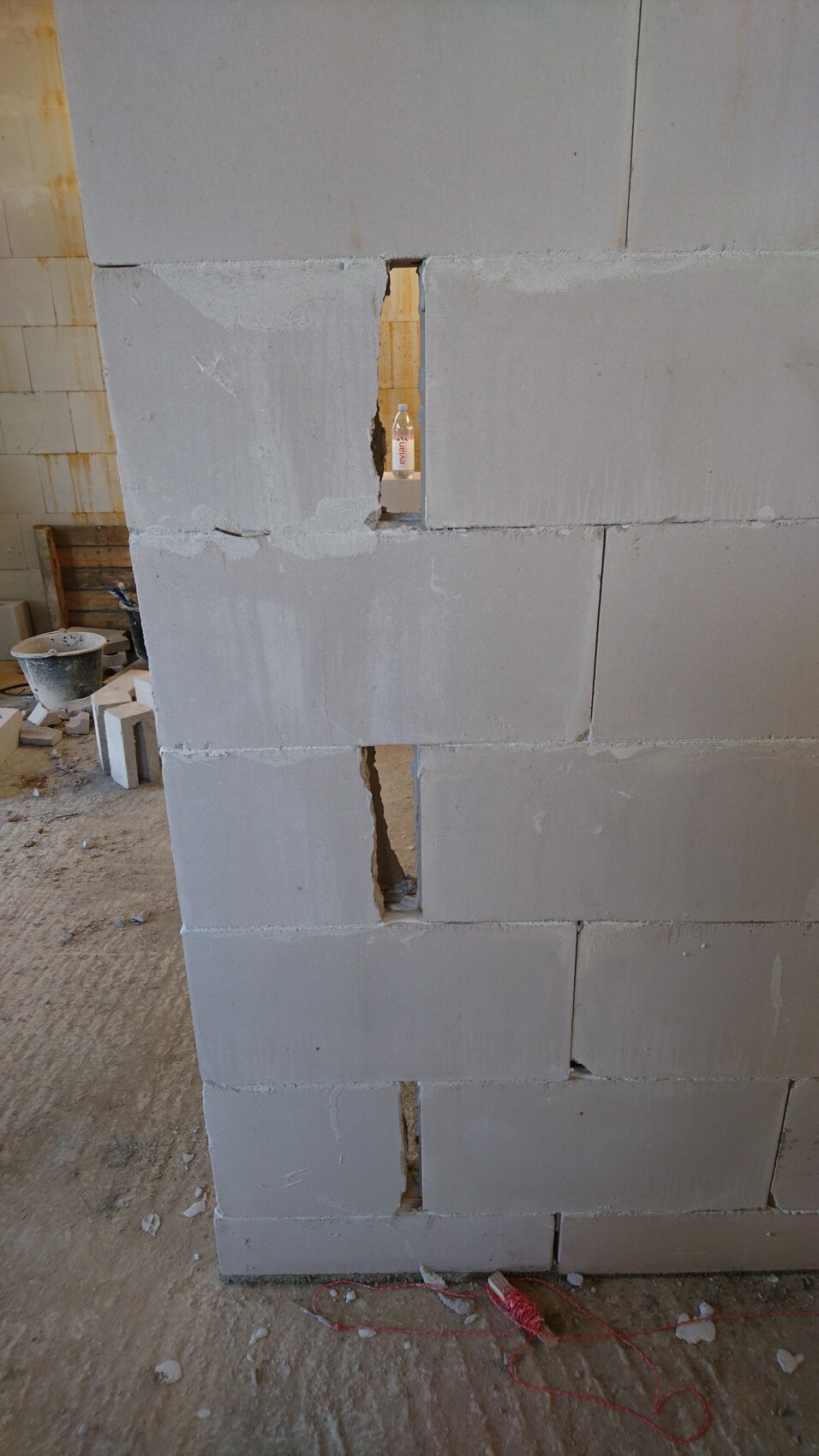 Betonblockwand mit vertikalen Löchern; durch ein Loch ist eine Wasserflasche sichtbar; Baustelle.
