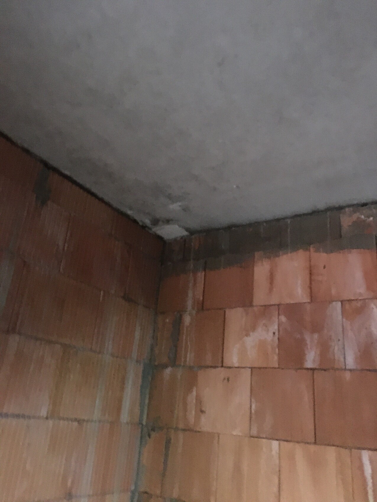 Eckraum mit offenen Ziegelwänden und roher Beton-Decke; Baustellenzustand.