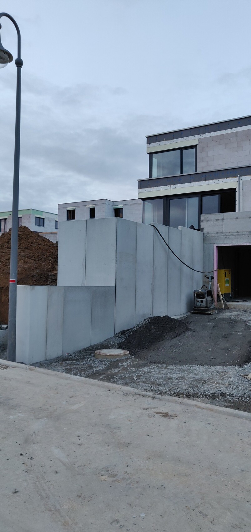 Baustelle mit Betonplattenmauer, modernem Mehrfamilienhaus, Baugerät, Kieshaufen.