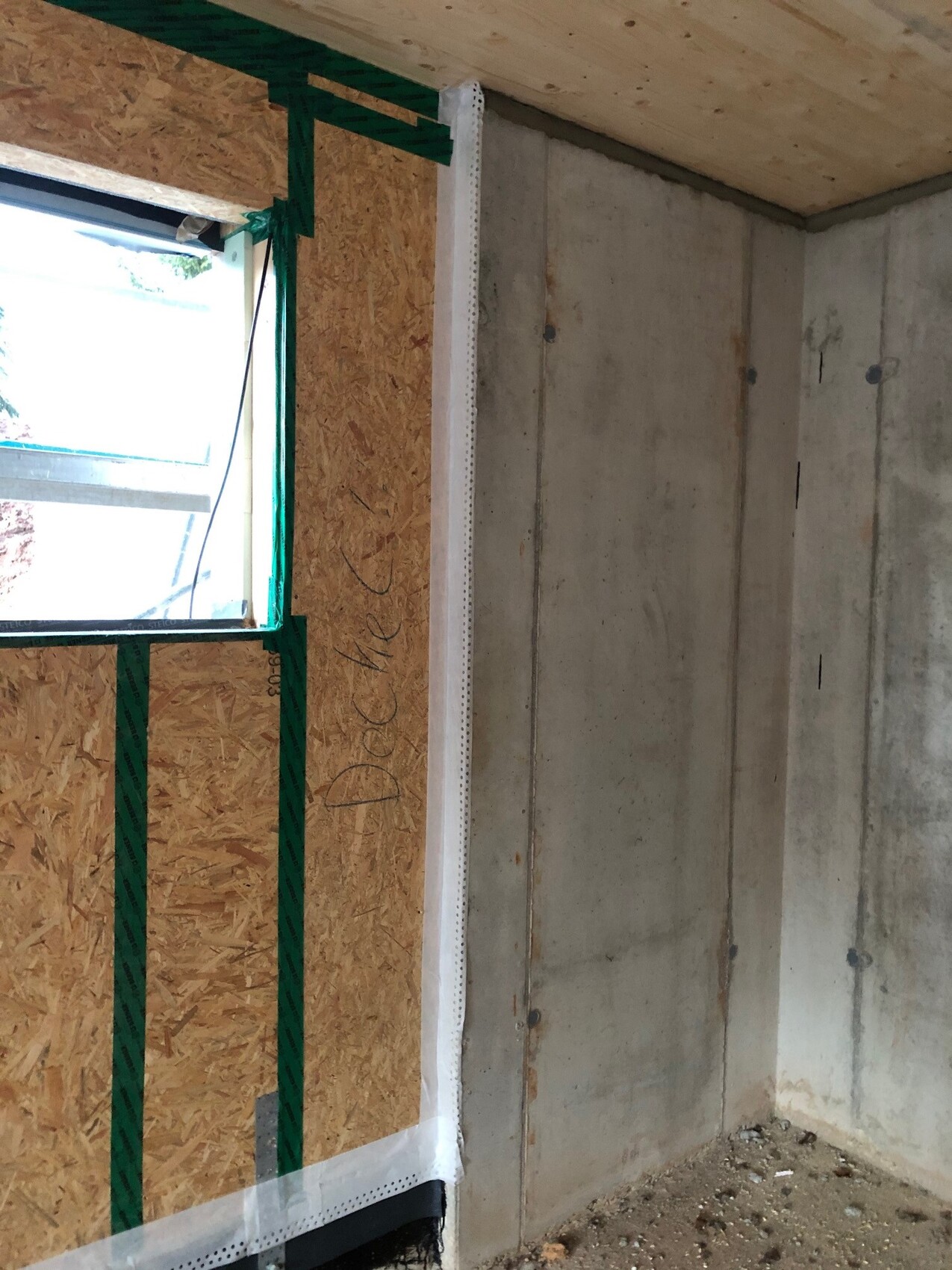Innenansicht eines Rohbaus: Betonwand rechts, OSB-Verkleidung links, Fensteröffnung.