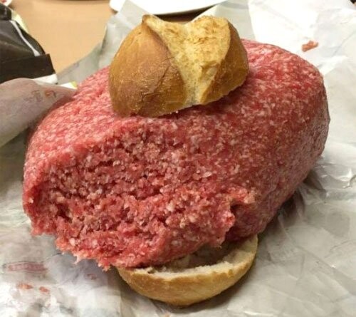 Rohes Hackfleisch-Patty zwischen zwei Brötchenhälften auf Backpapier.