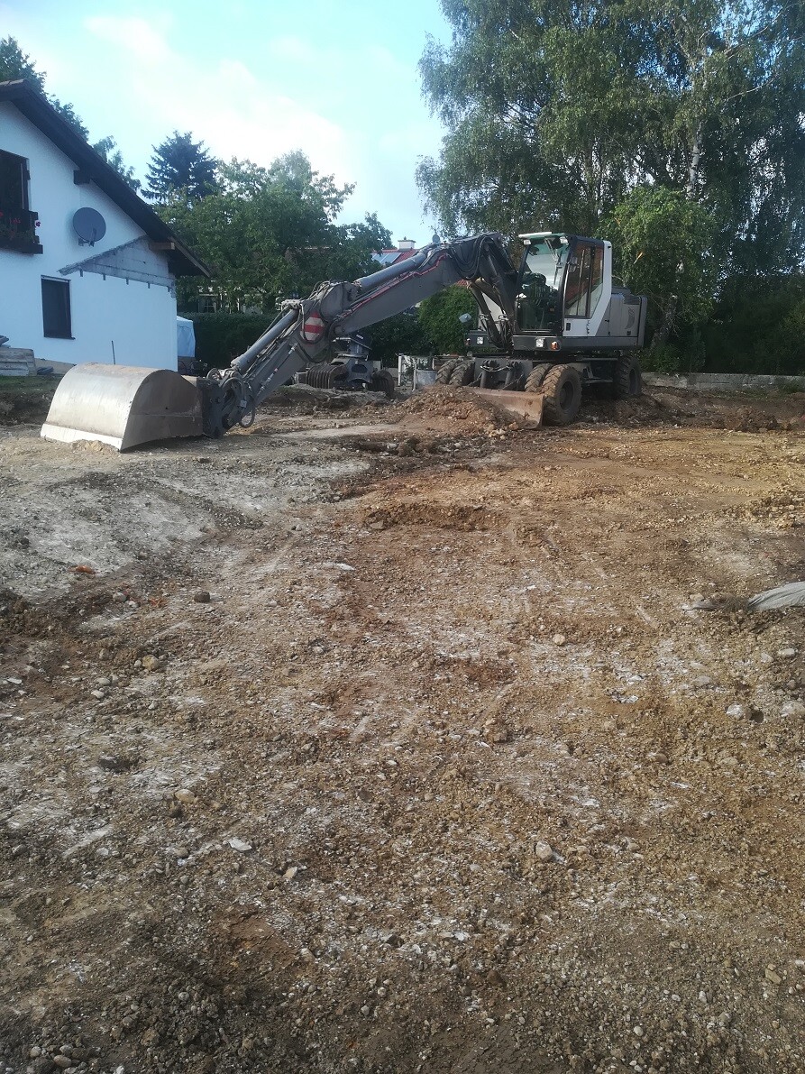 Baustelle mit Großbagger auf unbefestigtem Erdreich neben Einfamilienhaus