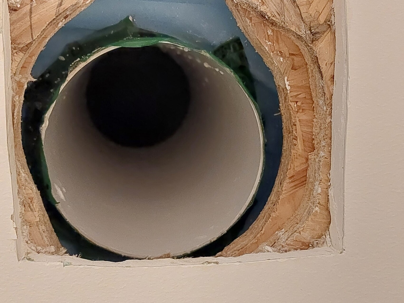 Rundes PVC-Rohr durch Wandöffnung mit Holzrahmen und grünem Rand.