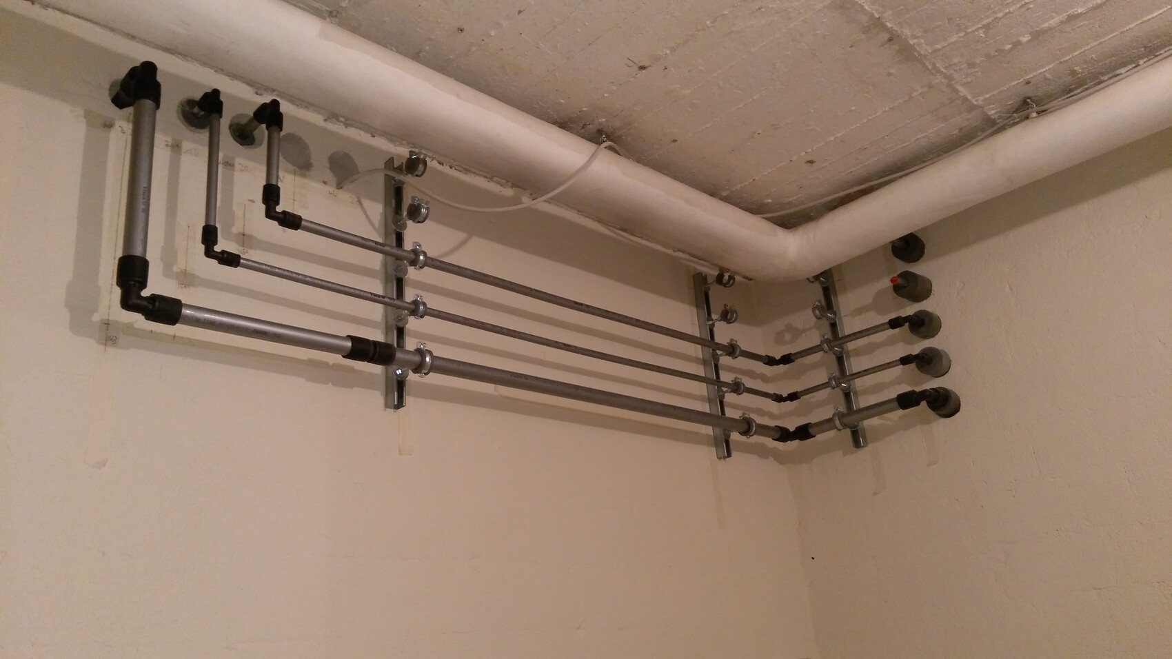 Kellerrohrinstallation: mehrere parallel verlaufende Metallrohre an Halterungen und eine PVC-Leitung