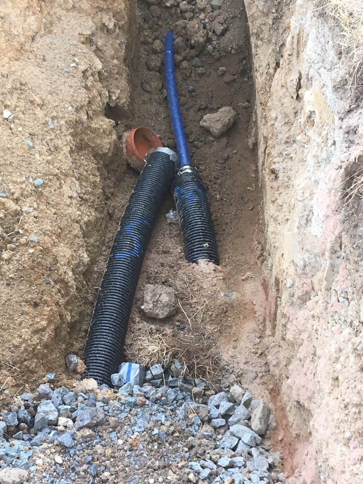 Graben mit blauen Rohrleitungen und Kies bei Bauarbeiten am Fundament