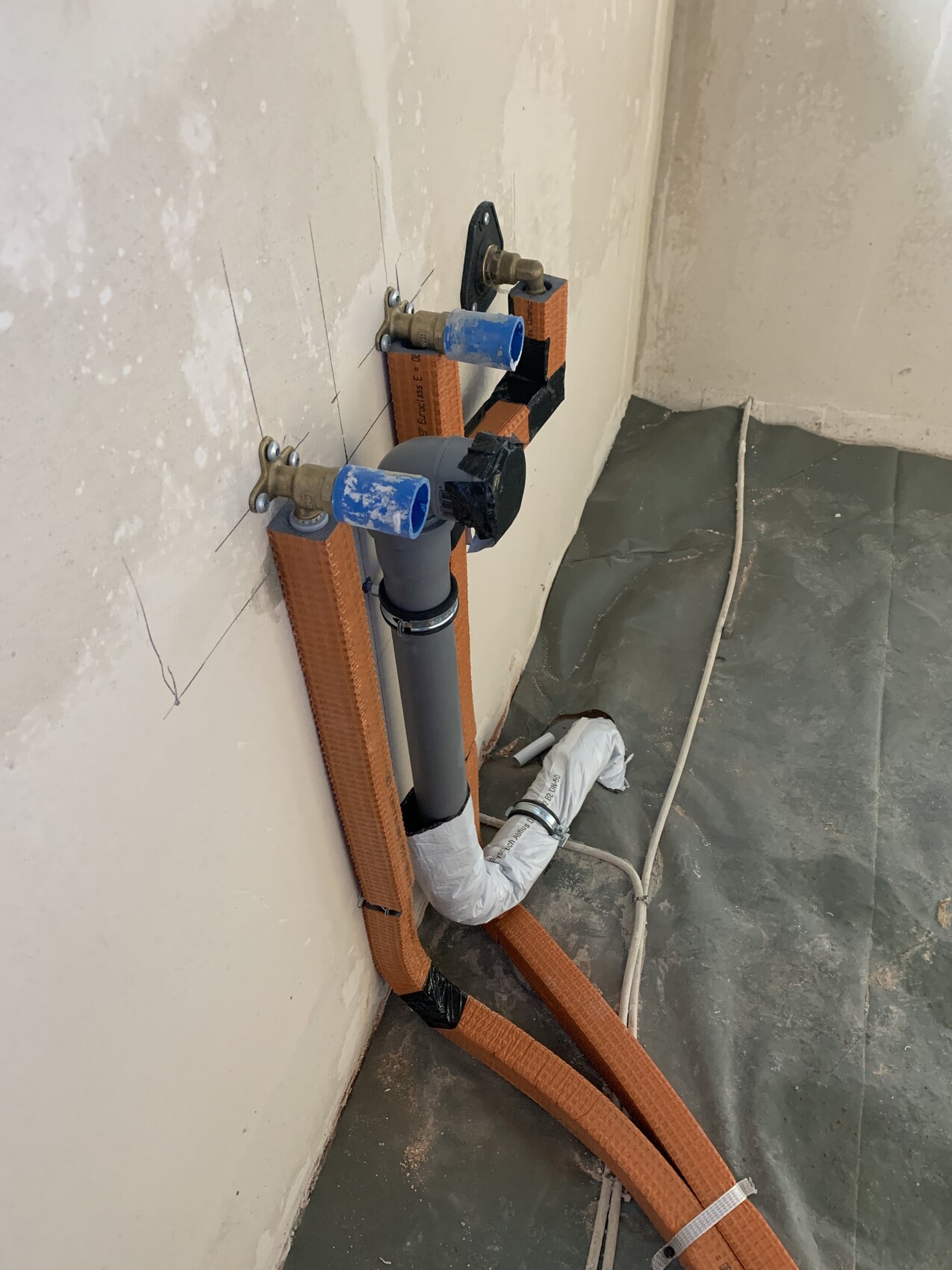 Abfluss- und Siphonrohr an der Wand, blaues Ventil, orange Bänder.