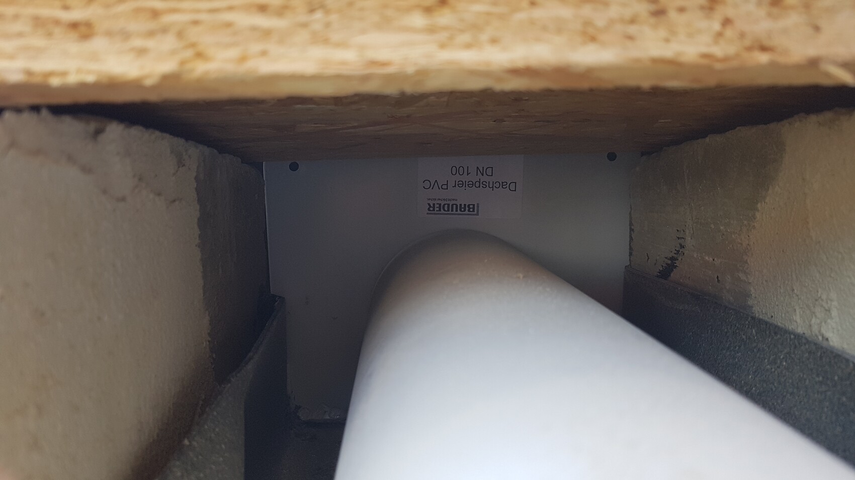 Enge Innenansicht eines PVC-Rohrbogens (90°) hinter Holzplatte und Wand.