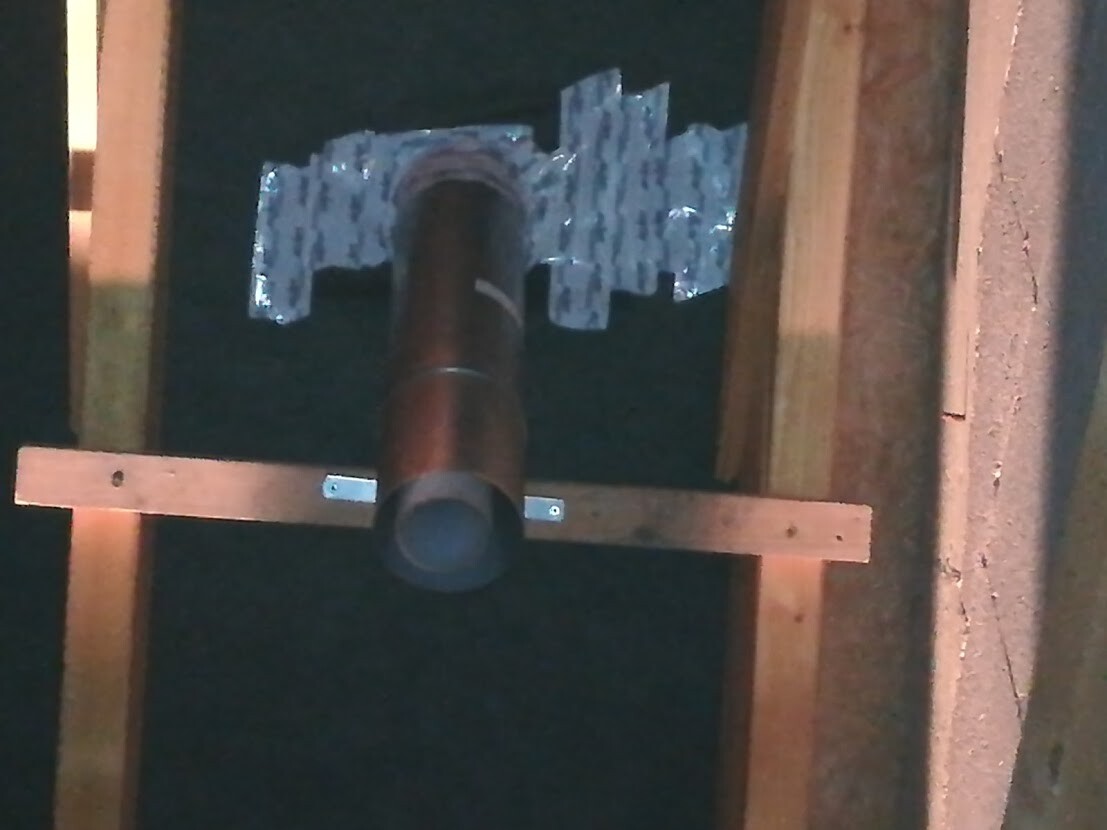Metallrohr durch Holzrahmen, dunkler Hintergrund, bläulich-graue Dämmung sichtbar.
