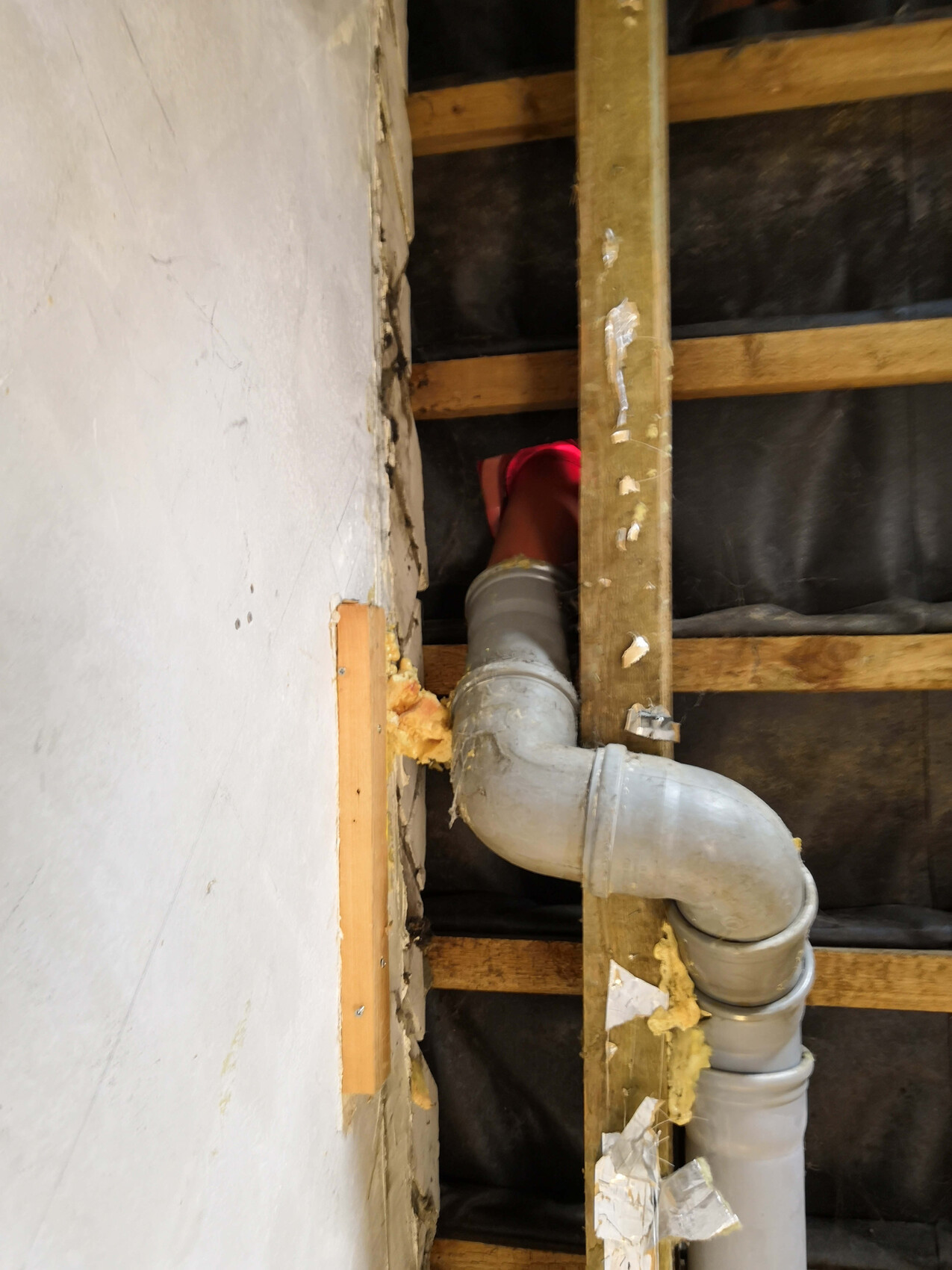 Metallrohrbogen in einer Wandkonstruktion aus Holzständern, freiliegende Dämmung sichtbar.