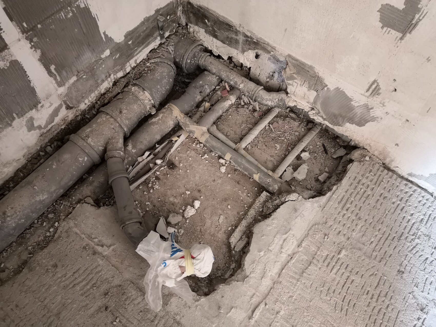 Offene Baugrube mit freigelegten Sanitärrohren, Staub und Müllreste.