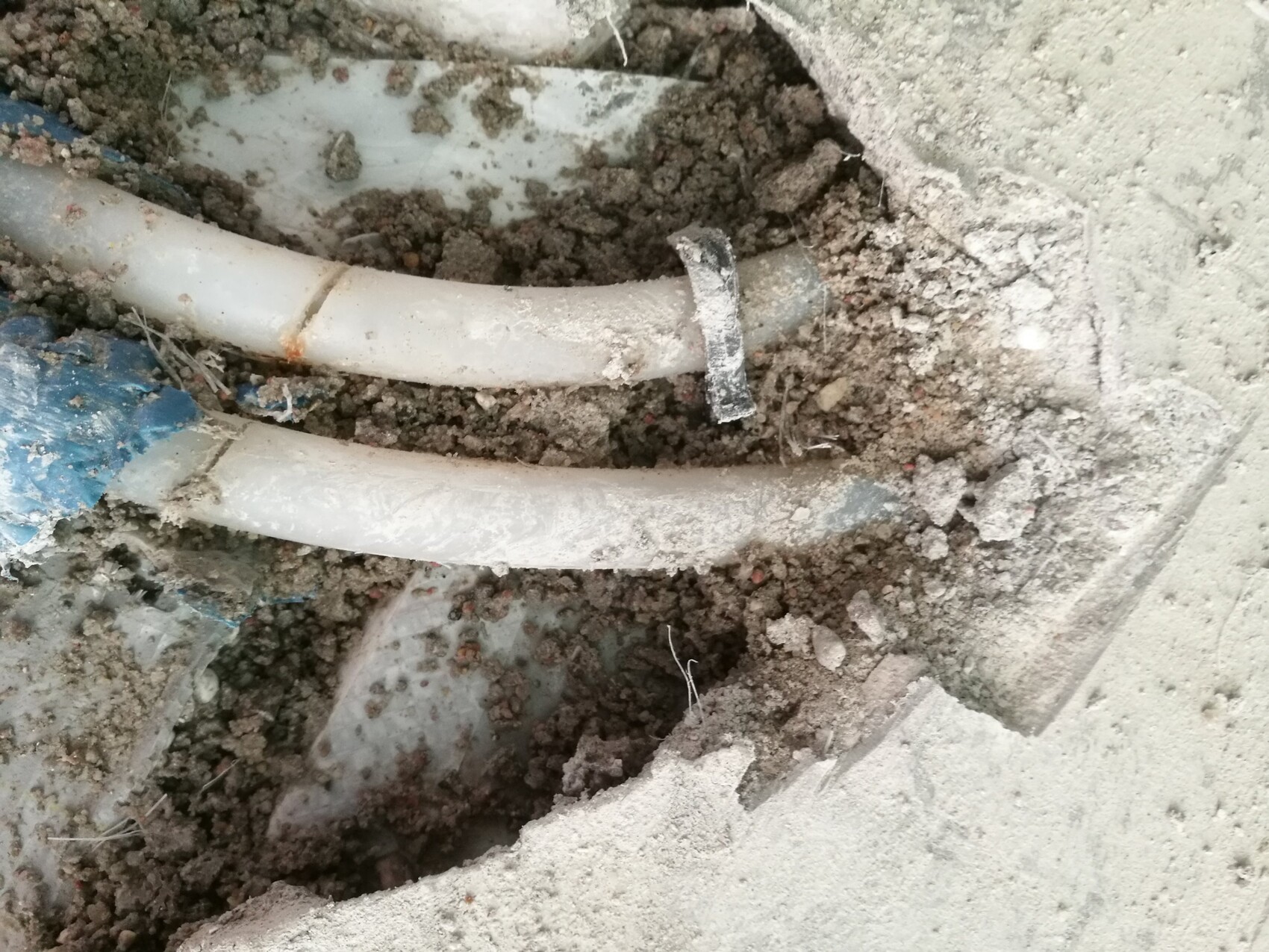 Kunststoffrohre im Erdreich während Bauarbeiten, Schutt und Betonboden sichtbar.