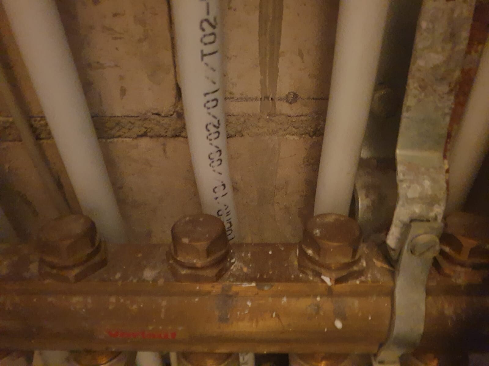 Mehrere Rohre (PVC) und eine Metallbandklemme an einer Holzbalkendecke im Keller.