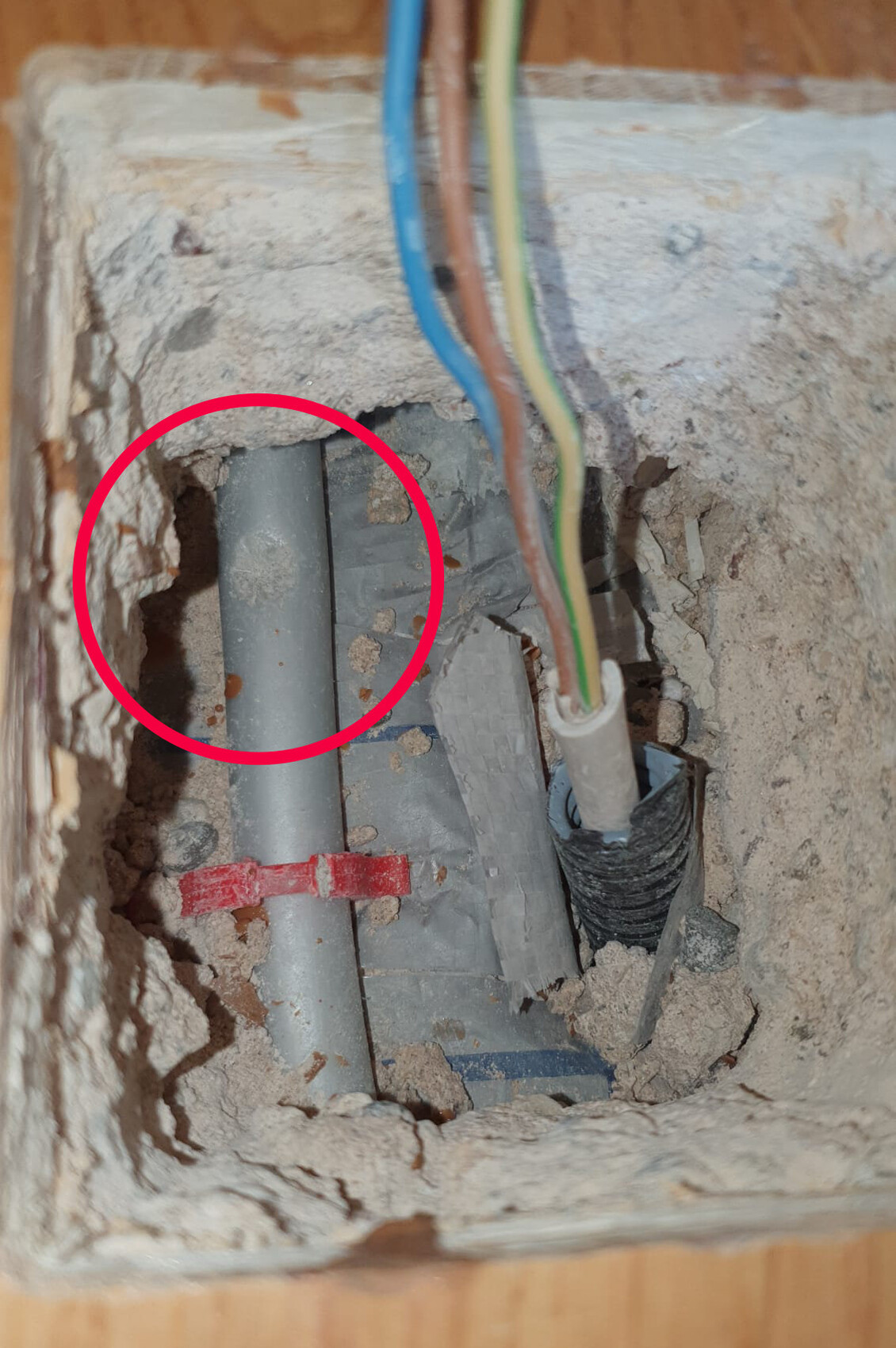 Grau PVC-Rohr in einer Wandöffnung, Staub und Kabelstränge daneben.