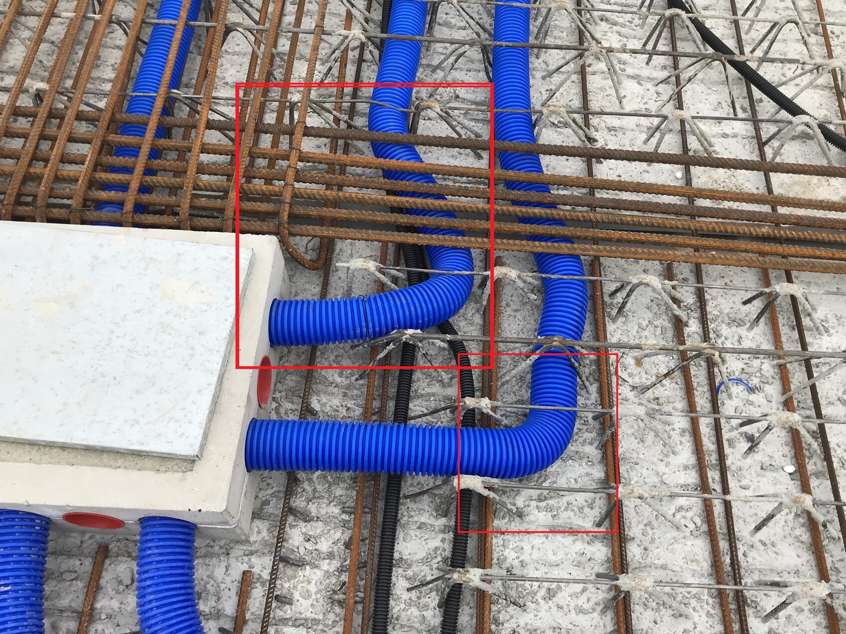 Baustelle: Blaue flexible Kabelkanäle verlaufen durch Bewehrungsstahl auf Betonboden.