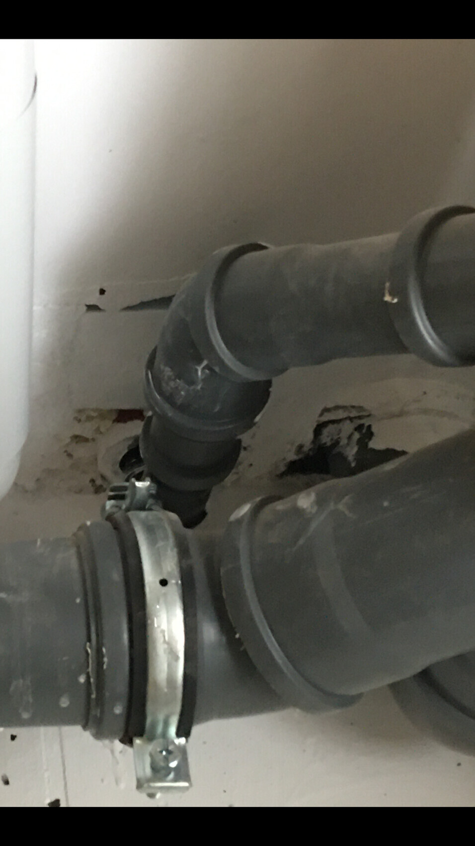 Grau-schwarze Kunststoffrohrleitung mit Bogenverbinder und Metallklemme.