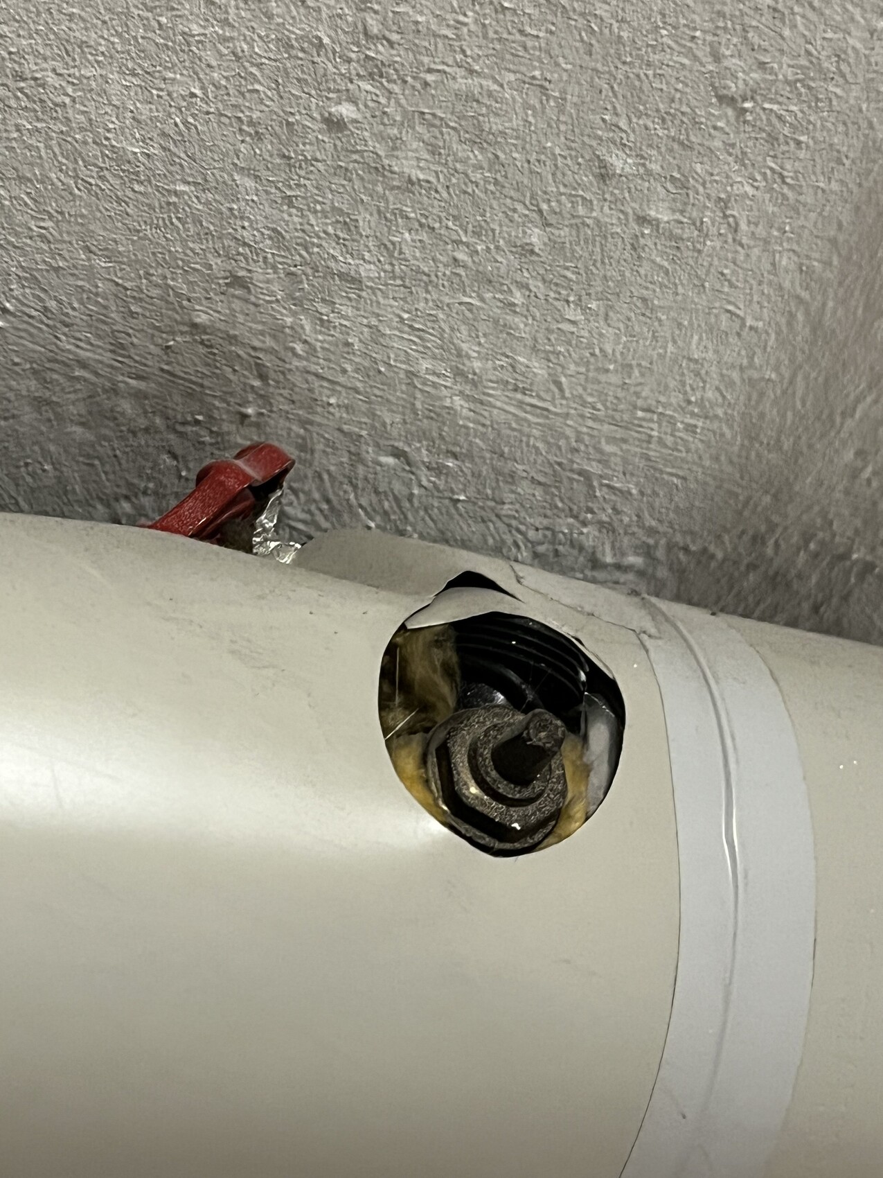 Nahaufnahme eines weißen Rohrs mit offener Öffnung; sichtbar ist ein Schraubenkopf/Bolzen und rotes Kabel dahinter.