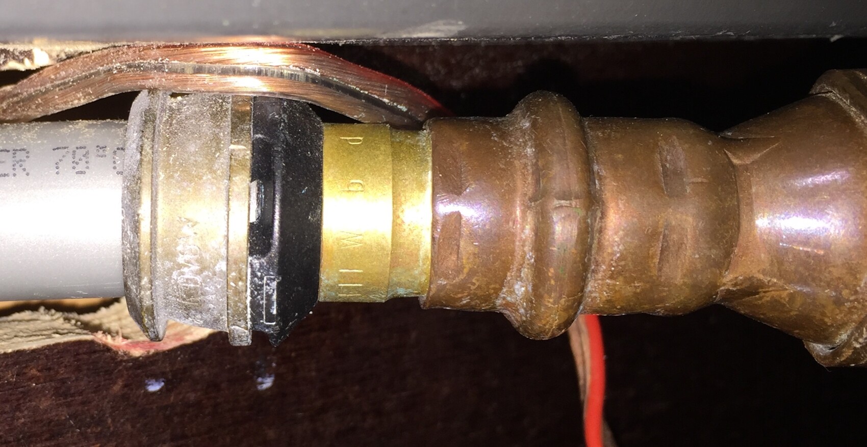 Nahaufnahme einer Rohrverbindung mit Kupferrohren und Messingfittings unter dem Spuelbecken