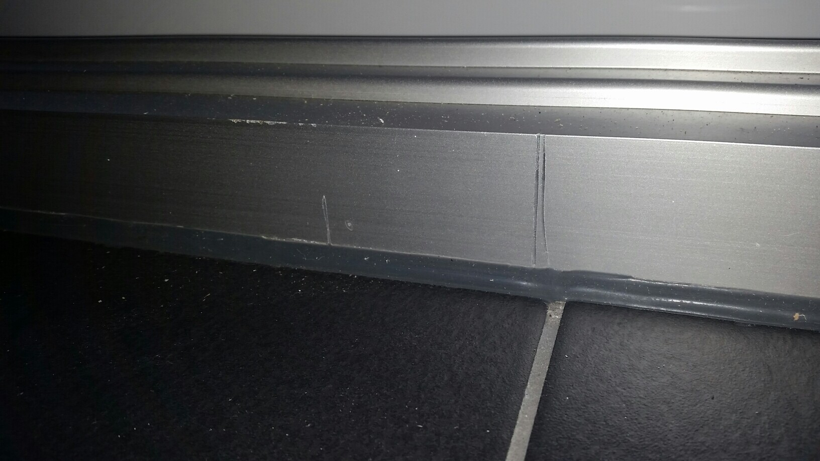 Nahaufnahme einer metallischen Rollladenunterkante über dunklem Bodenbelag
