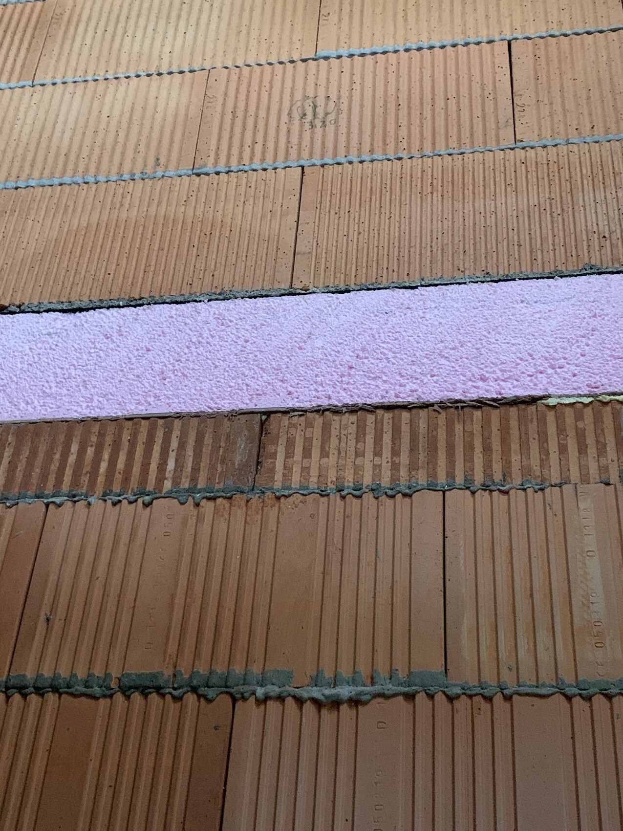 Nahaufnahme von braunen Dachziegeln mit rosa Dämmstoffstreifen zwischen den Reihen.