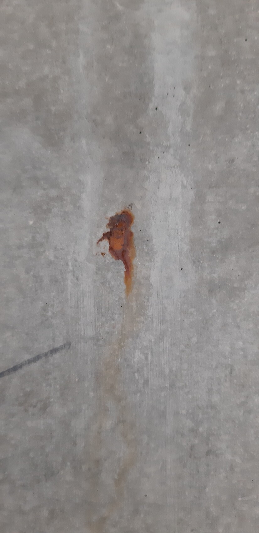Kleiner rostbrauner Fleck auf grauer Betonoberfläche, orangebraune Verfärbung.