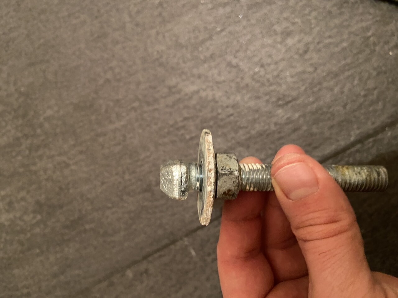Rostige Schraube und Mutter in einer Hand vor grauem Hintergrund