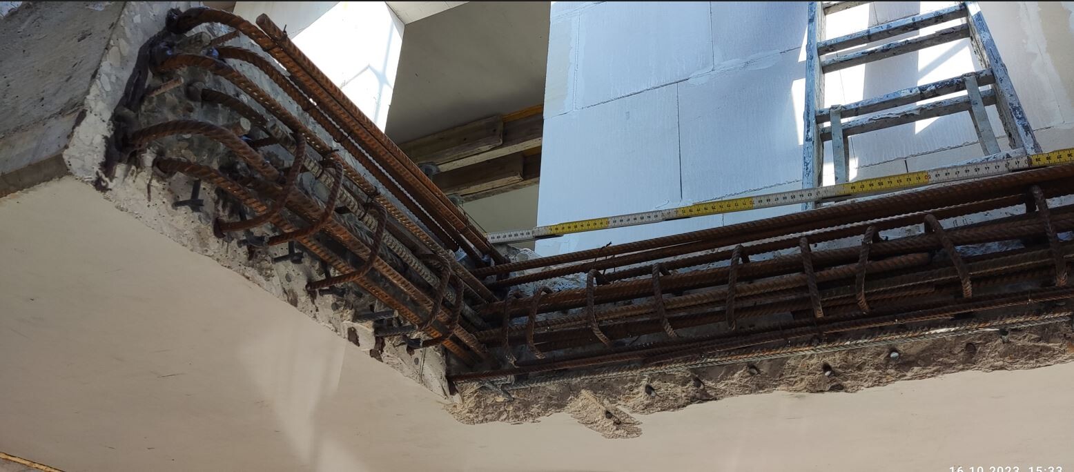 Rostige Bewehrungsstähle im offenen Betonbalken; Leiter und Maßband liegen daneben.