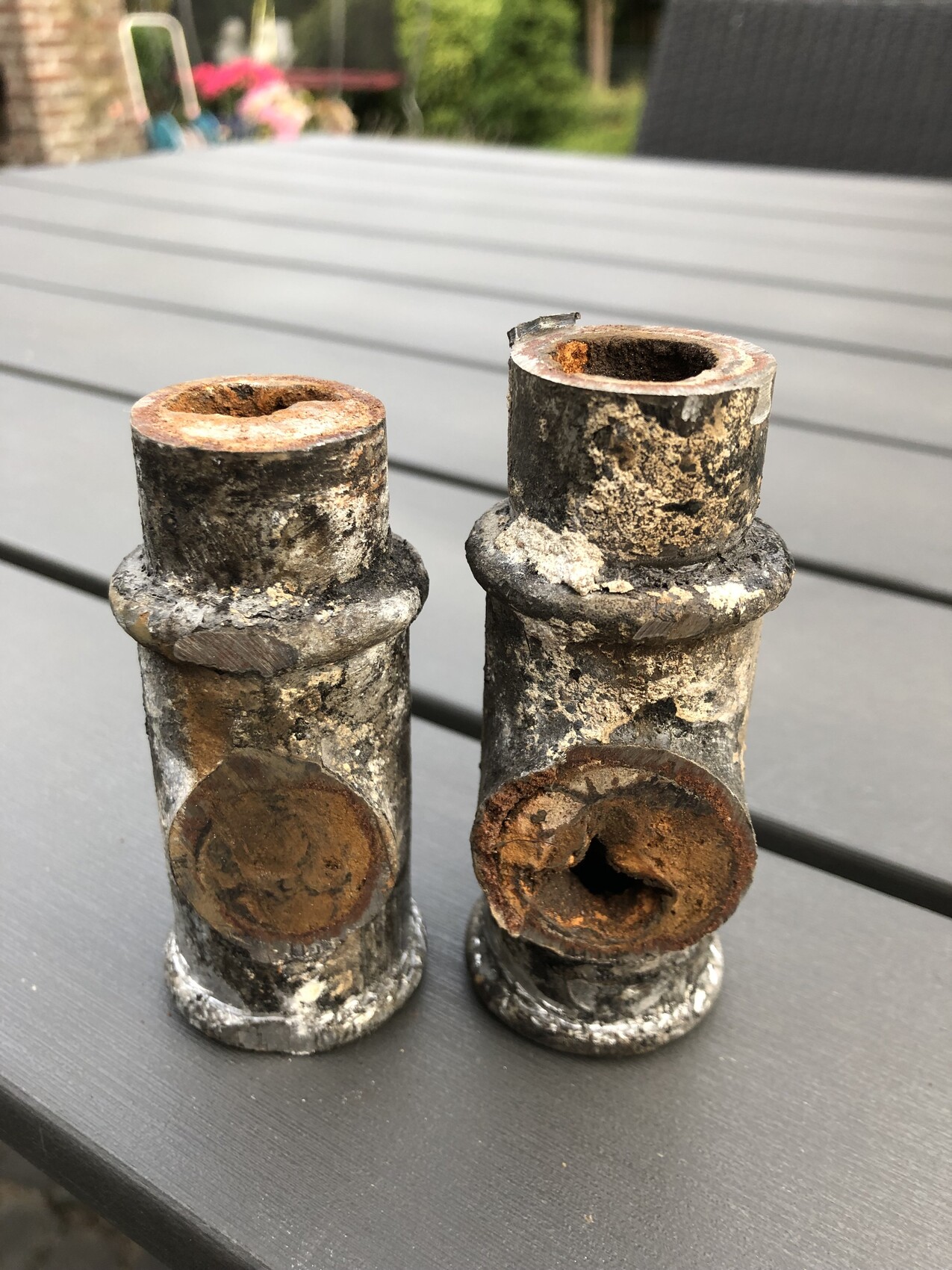 Zwei rostige Rohrstutzen stehen auf einer Terrasse, stark korrodiert und verschmutzt.