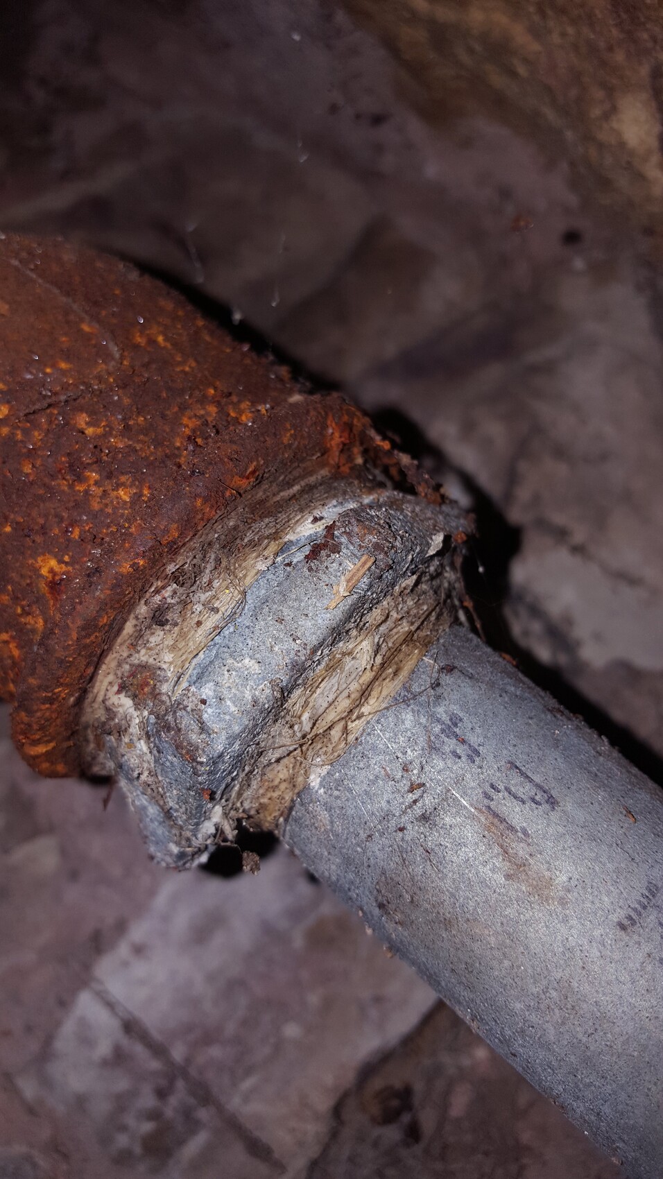 Nahaufnahme eines rostigen Metallrings um ein graues Rohrstück in dunkler Umgebung.