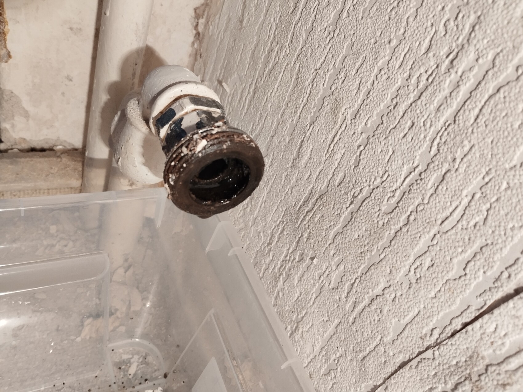 Verrostetes Rohrende mit dunkler Innenfläche, an einer rauen weißen Wand.