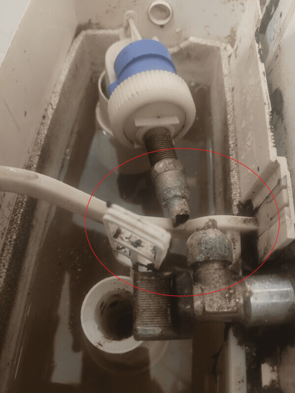 Verrostete Verschraubung und Schlauchverbindung im Spülkasten einer Toilette.